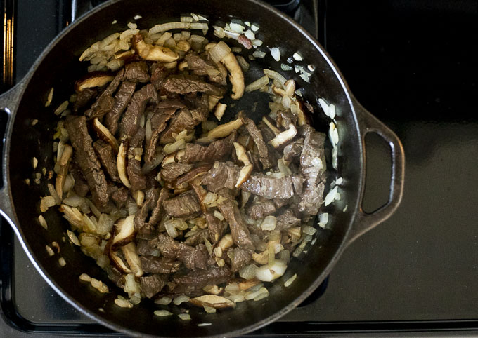 onions, mushrooms and beef slices cooking in a pot