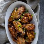 a plate of glazed chicken wings with sesame seeds and green onions