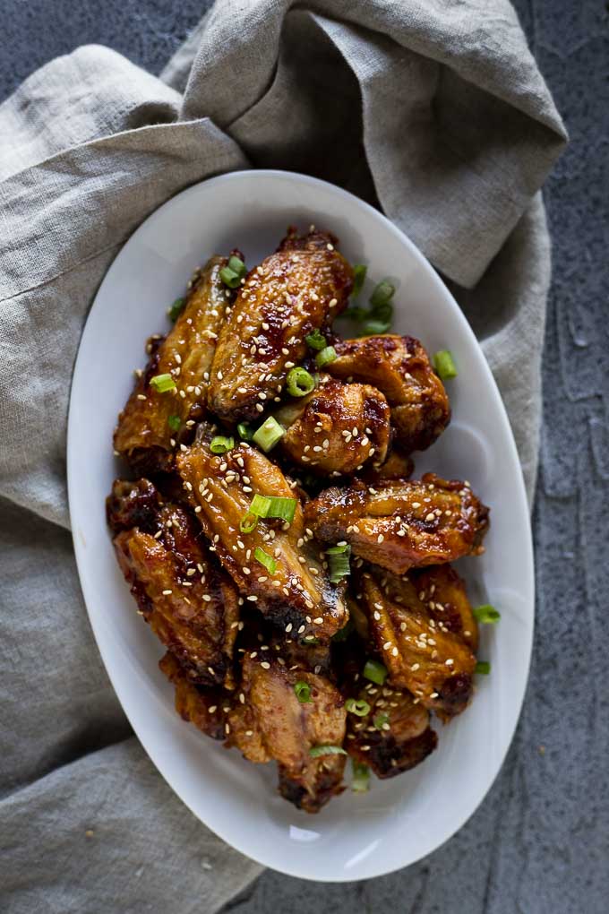 a plate of glazed chicken wings with sesame seeds and green onions