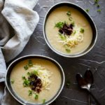 2 bowls of white cauliflower soup garnished with bacon, cheese and green onions