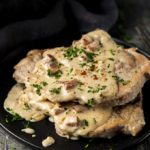 2 pork chops on a plate smothered in creamy sauce