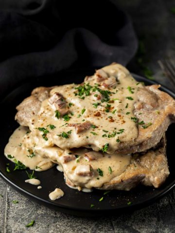 2 pork chops on a plate smothered in creamy sauce