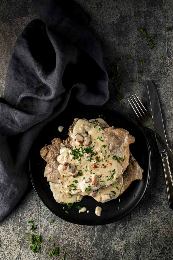 pork chops on a plate with cream gravy and utensils on the side