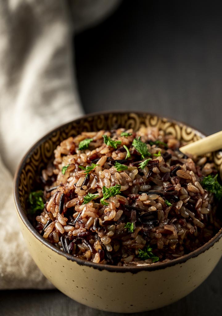 a bowl of wild rice with a gold spoon in it