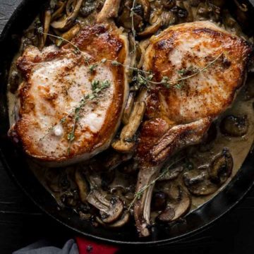 2 cooked pork chops in a skillet with mushrooms