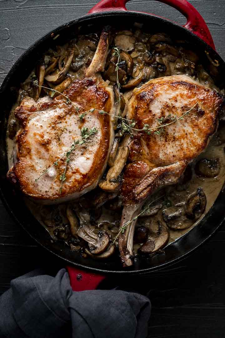 2 cooked pork chops in a skillet with mushrooms