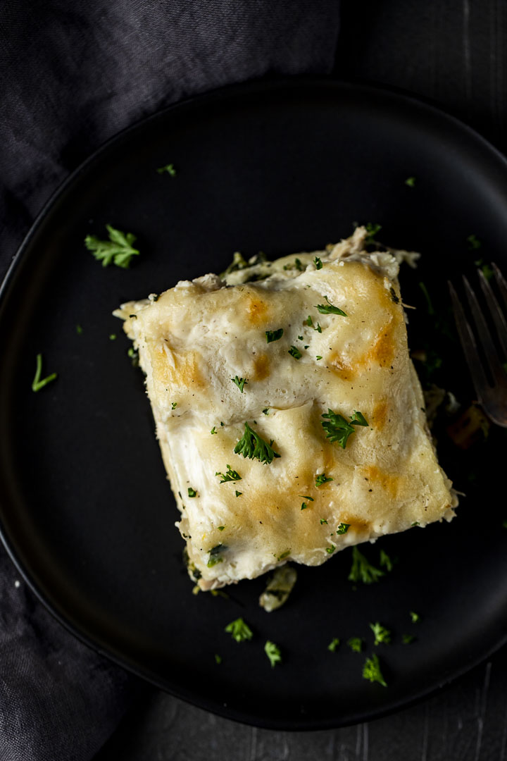 piece of white lasagna on a plate garnished with parsley