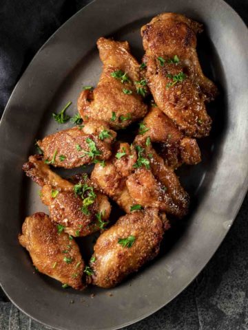 a plate of chicken wings in sauce sprinkled with parsley