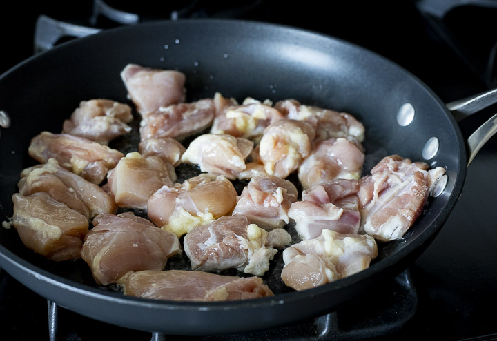 pieces of raw chicken cooking in a skillet