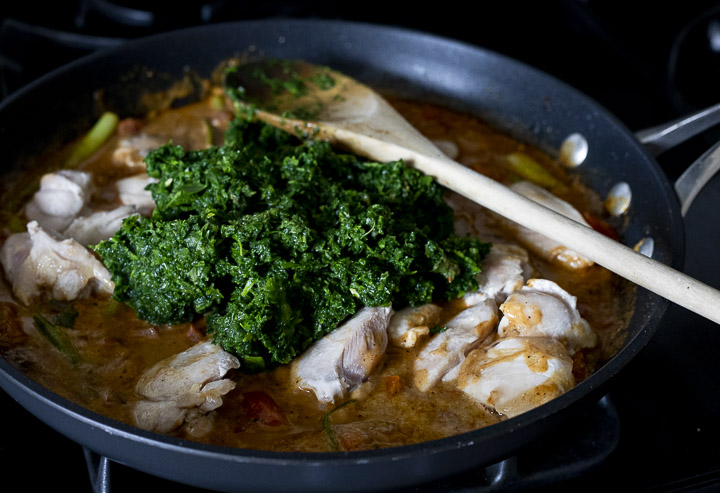 chicken pieces and spinach in a orang colored cream sauce in a skillet.
