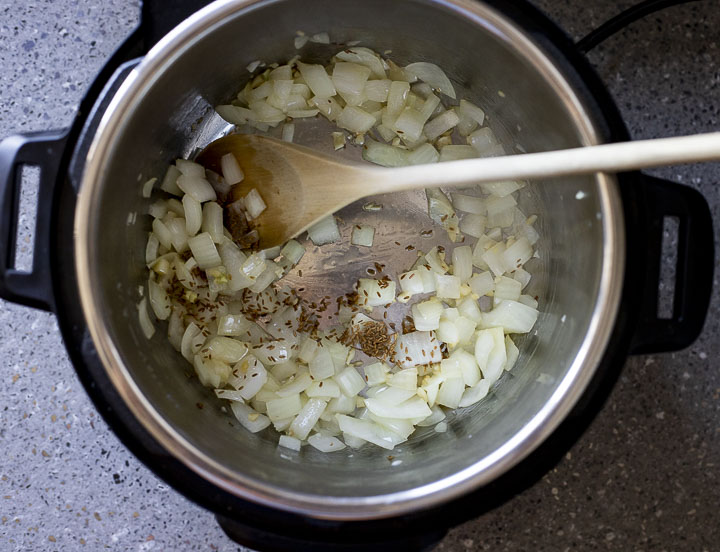 onions sauteing in a pot with whole cumin seeds