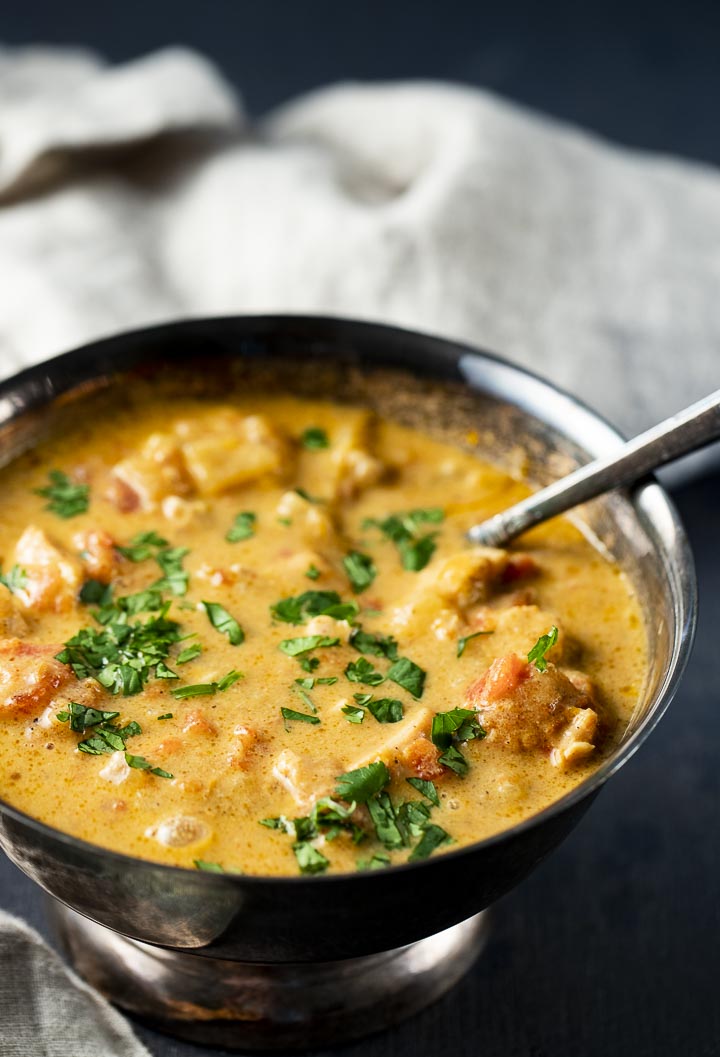 a bowl of orange colored chicken curry topped with cilantro