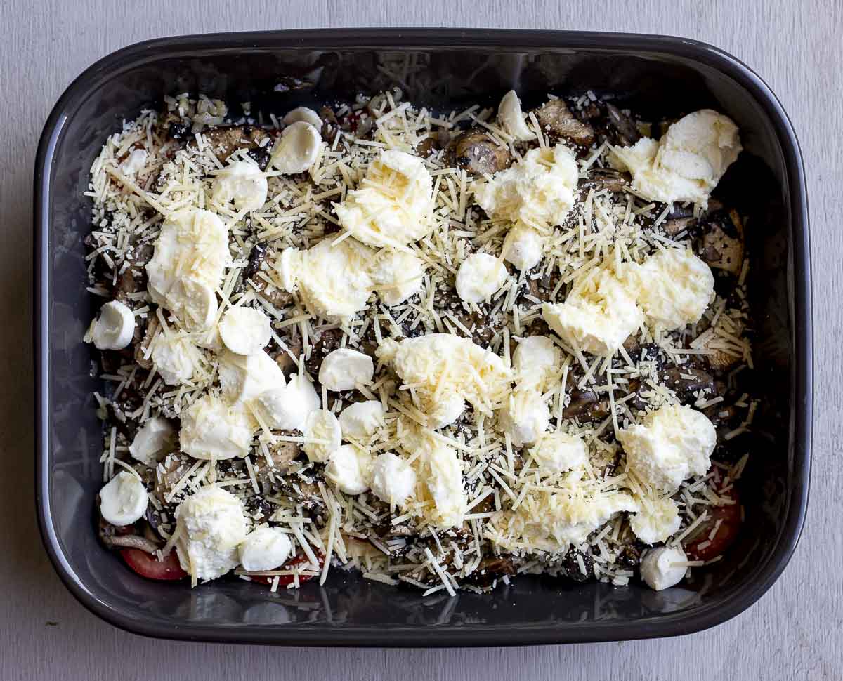 grated and pieces of cheese over mushroom in a baking dish