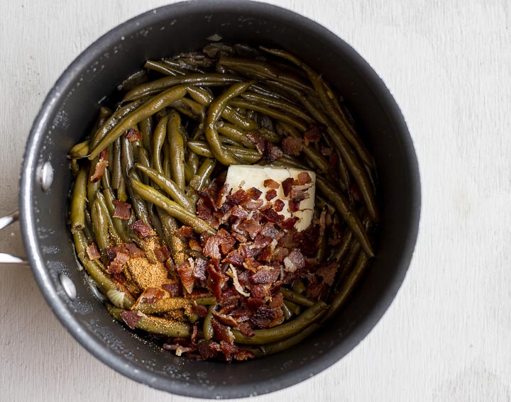cooked green beans with seasoning, butter and crumbles bacon in a pot