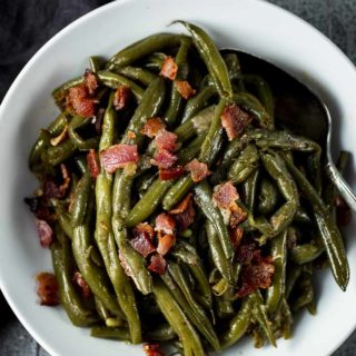 a bowl with cooked green beans and bacon with a spoon