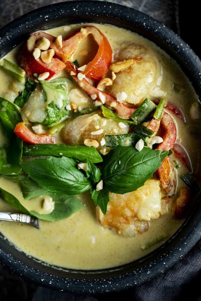 a bowl of green shrimp curry with peppers and fresh basil