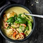 a bowl of curry shrimp and vegetables with a spoon