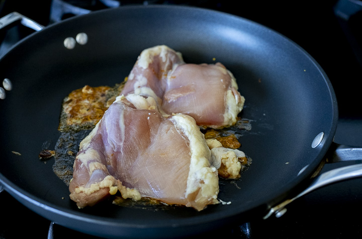 raw chicken thighs being cooked in a skillet