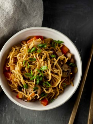 bowl of yellow noodles with diced red peppers and green onions on top