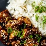 Close up view of air fryer sesame chicken served with rice and garnished with sesame seeds and green onions.