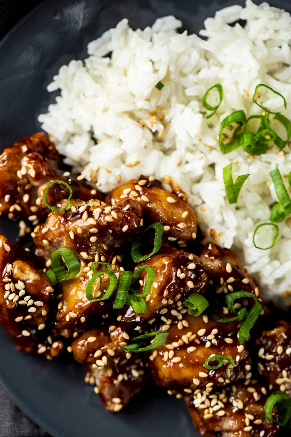 Close up view of air fryer sesame chicken served with rice and garnished with sesame seeds and green onions.