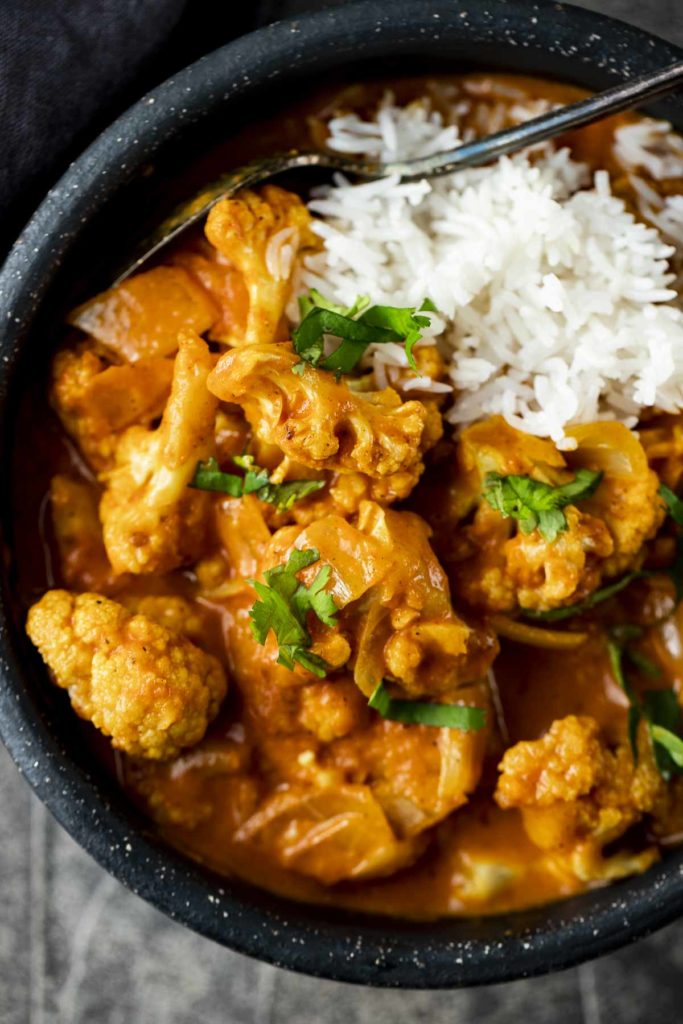 a bowl of cauliflower tikka masala in an orange curry sauce garnished with cilantro