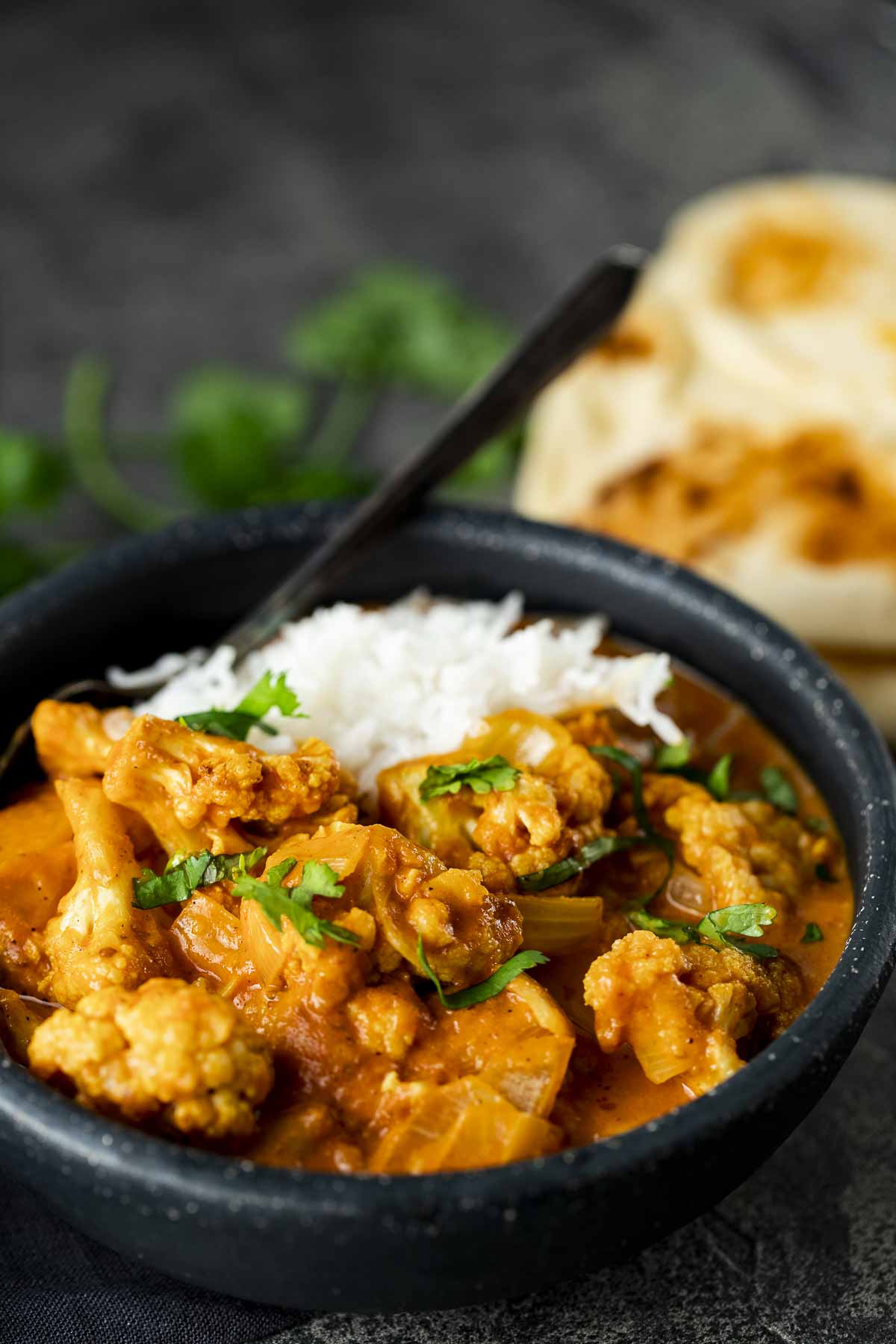 orange cauliflower curry in a bowl with rice and naan in the background