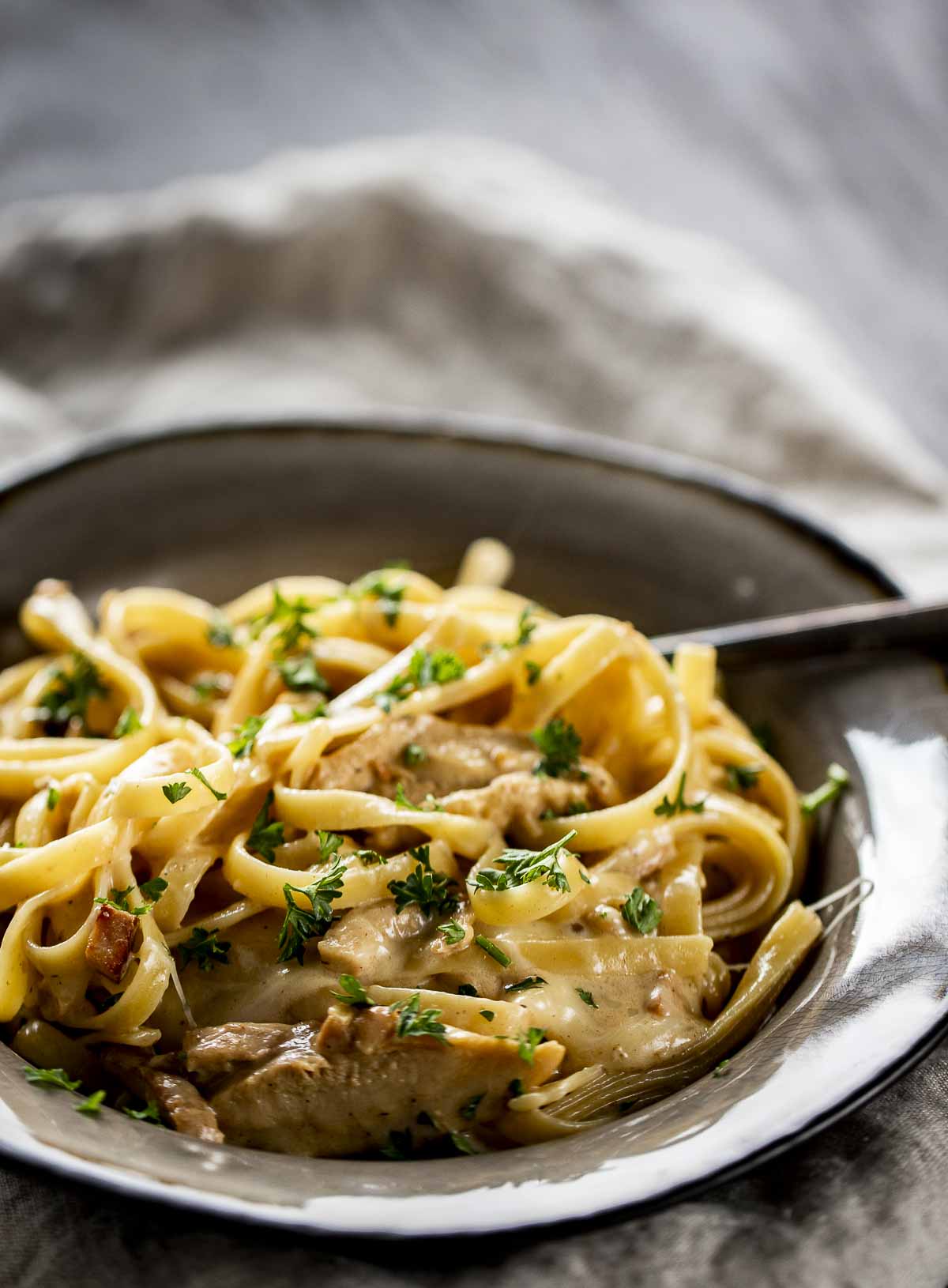 side view of a bowl of pasta in a creamy white sauce with chicken garnished with parsley