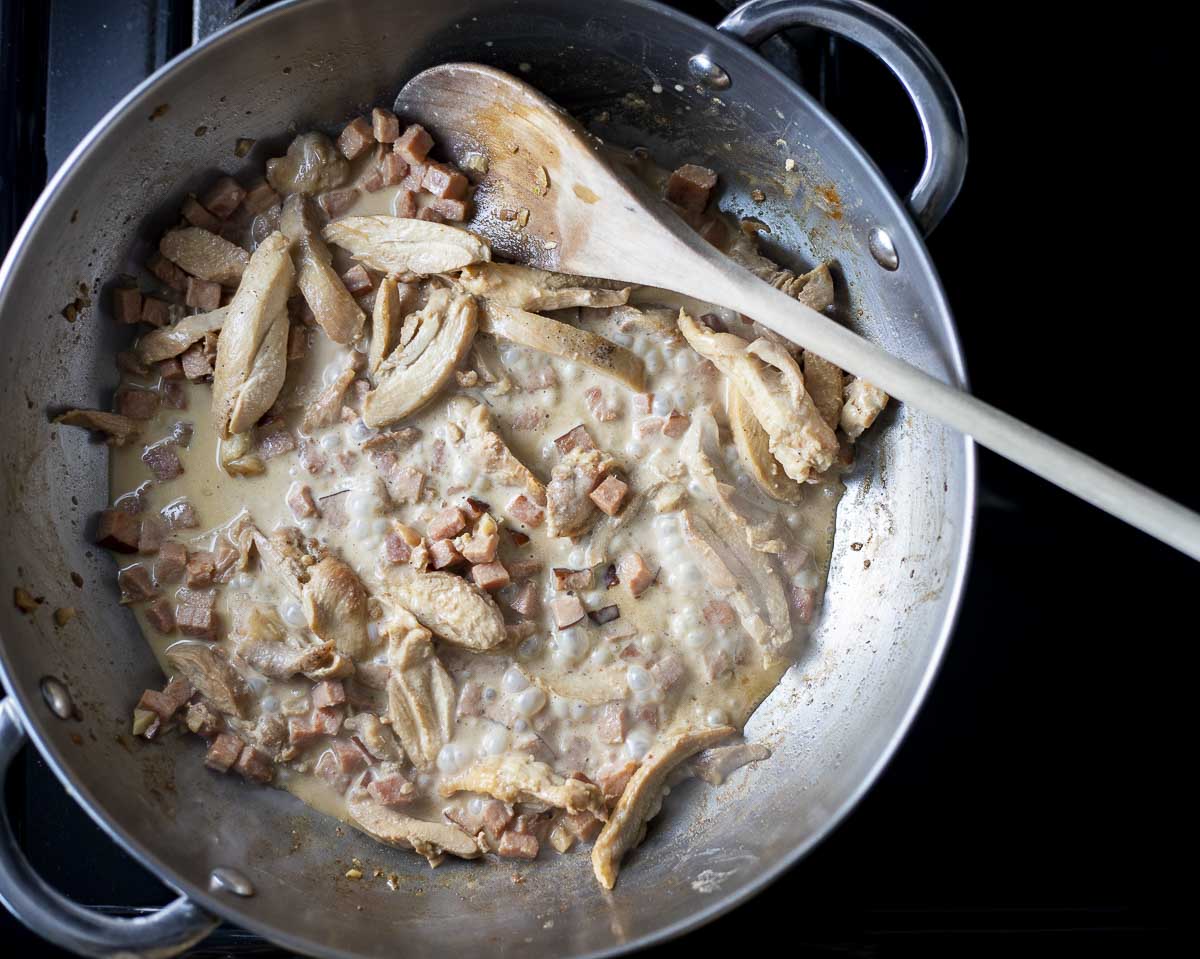 chicken slices and diced ham in a creamy white sauce in a skillet
