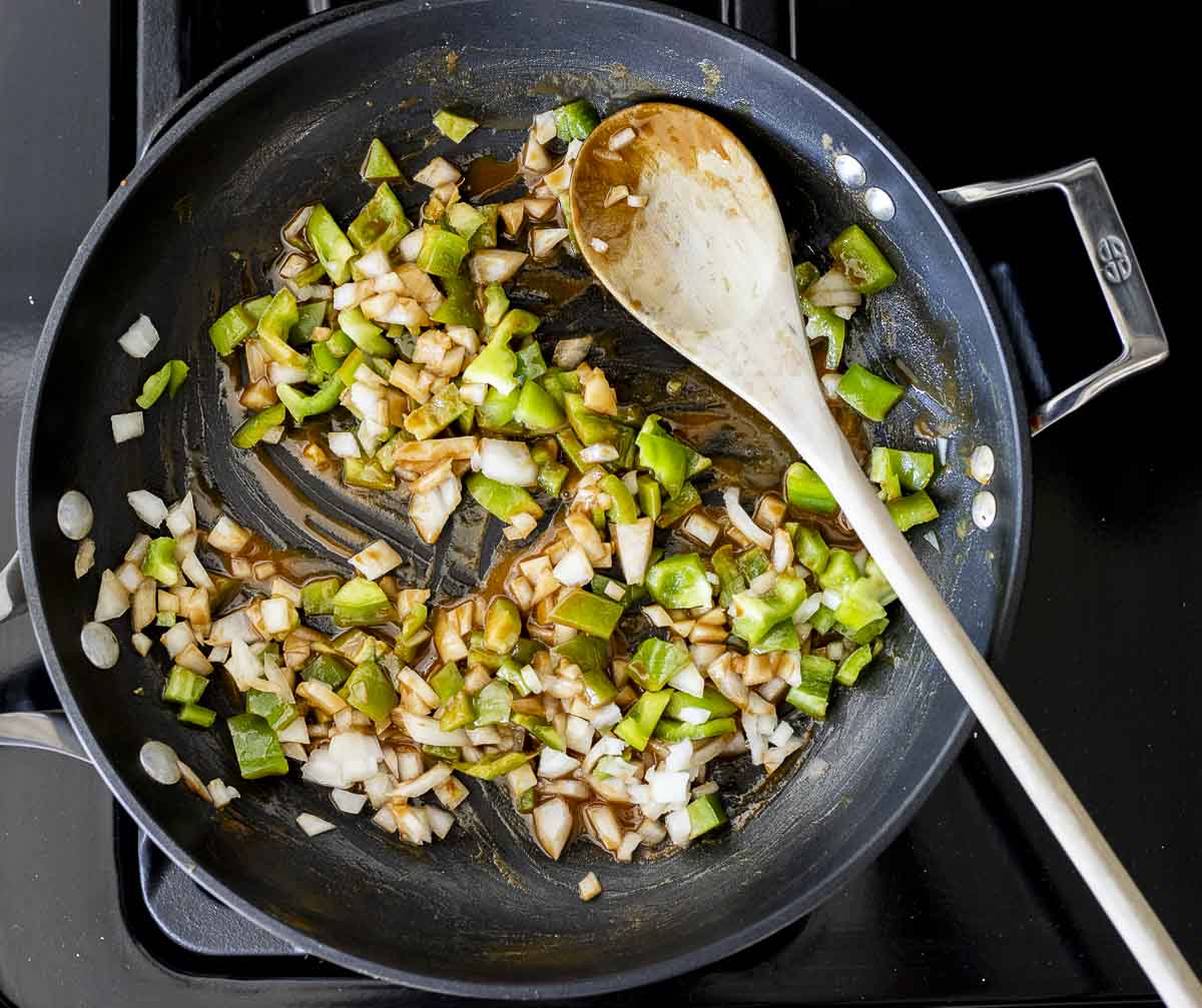 diced green peppers and onions sautéing in a skillet