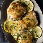 chicken thighs on a plate with creamy sauce and lemon slices