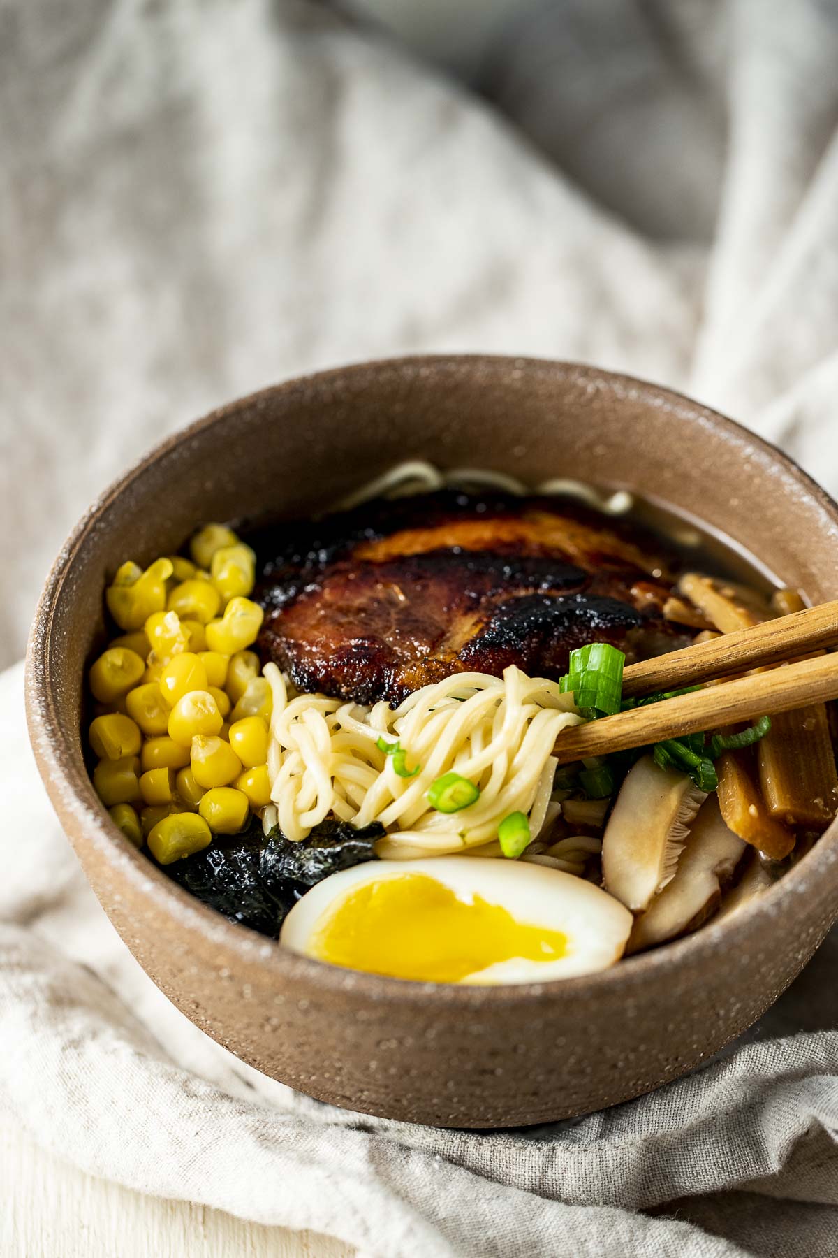 Shio ramen in a bowl topped with corn, ramen egg and braised pork.