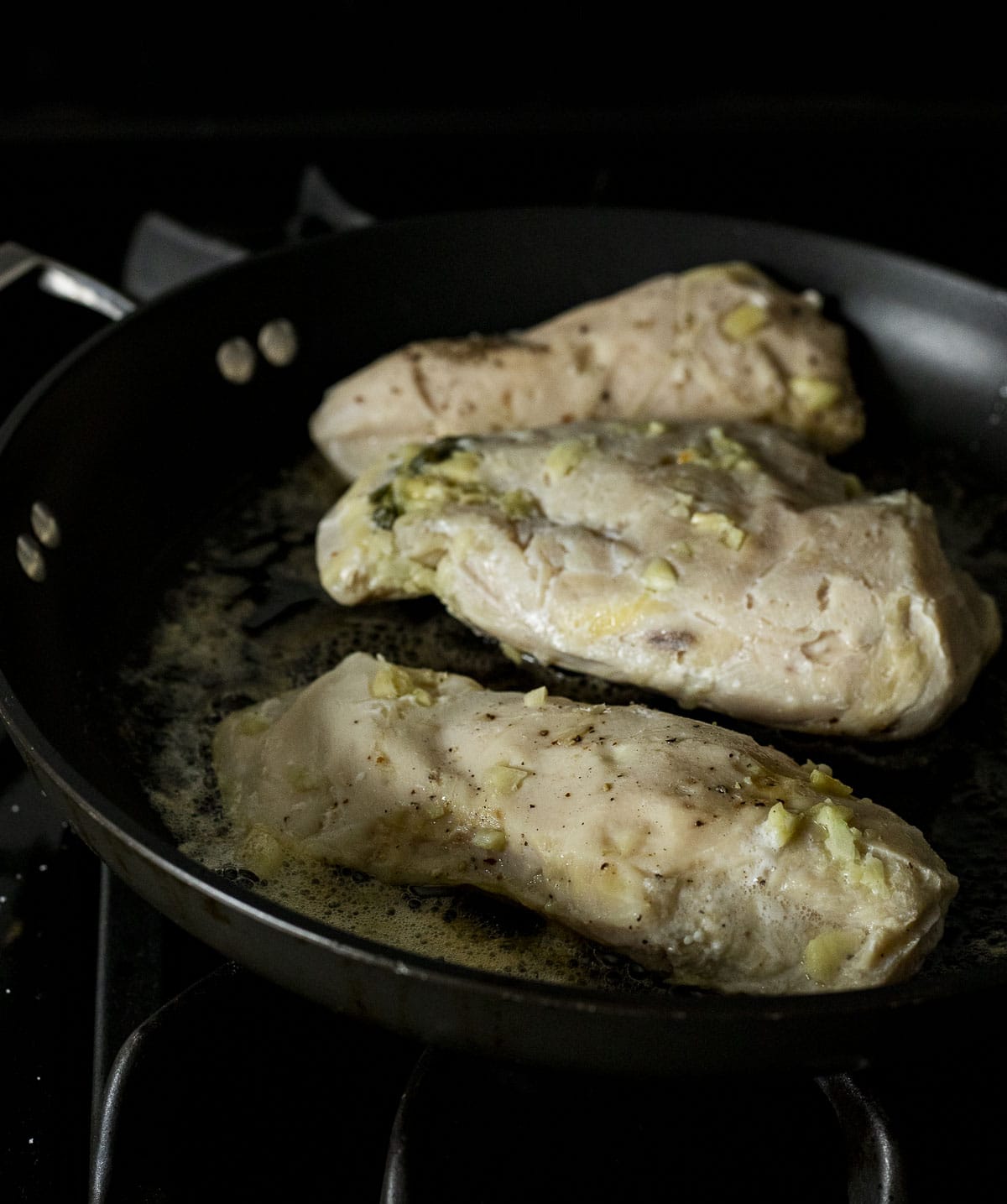 Chicken breasts browning in a skillet with melted butter.