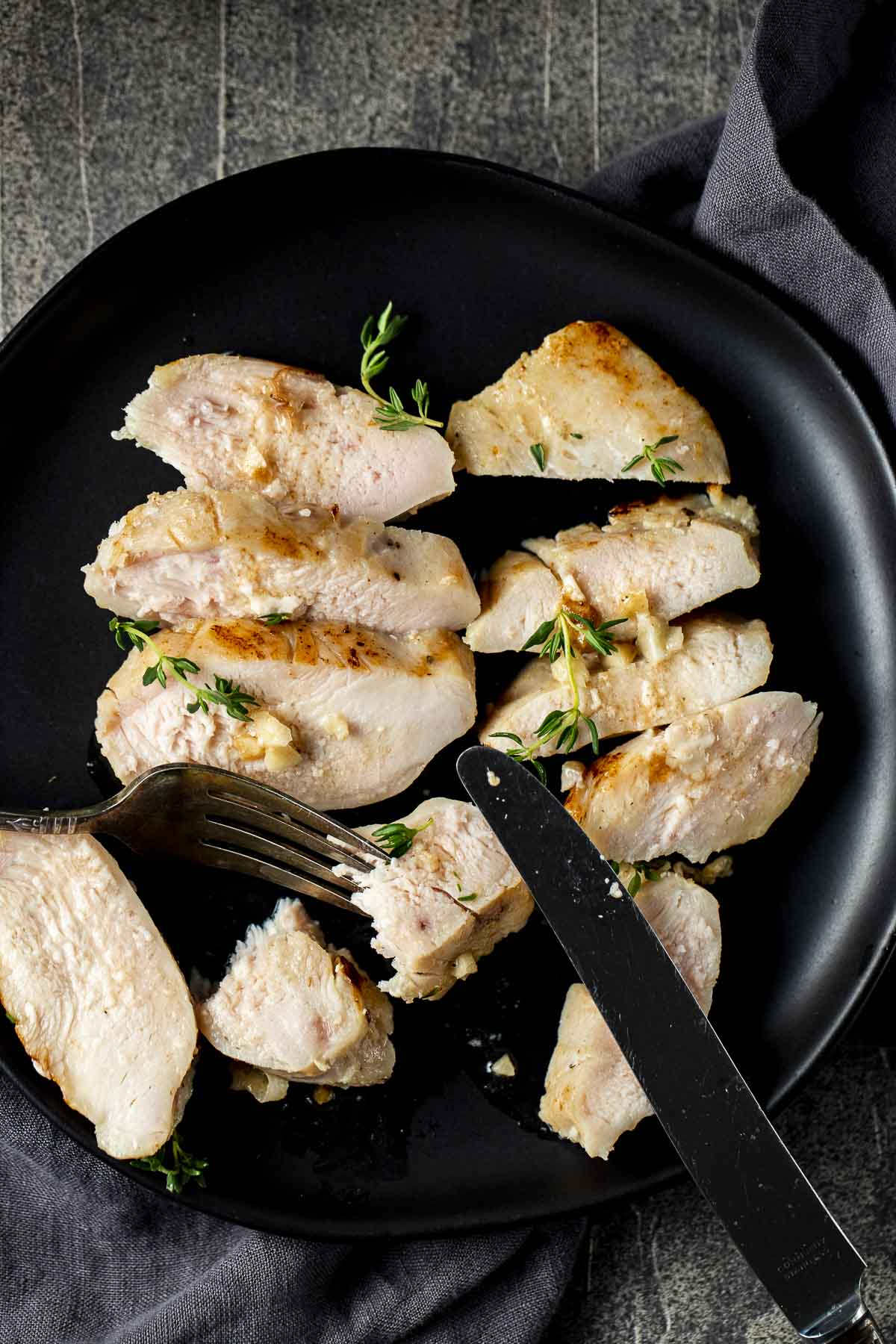 Overhead view of sliced chicken breast on a black plate with a fork.