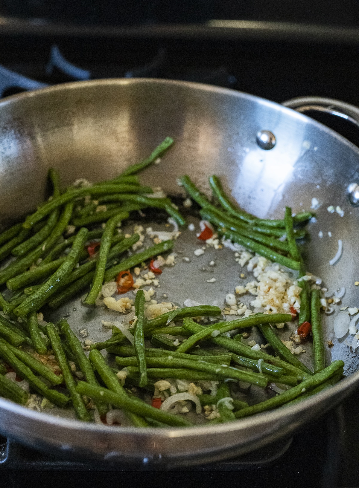 Garlic, shallot, long beans and chilis being sautéed in a wok.