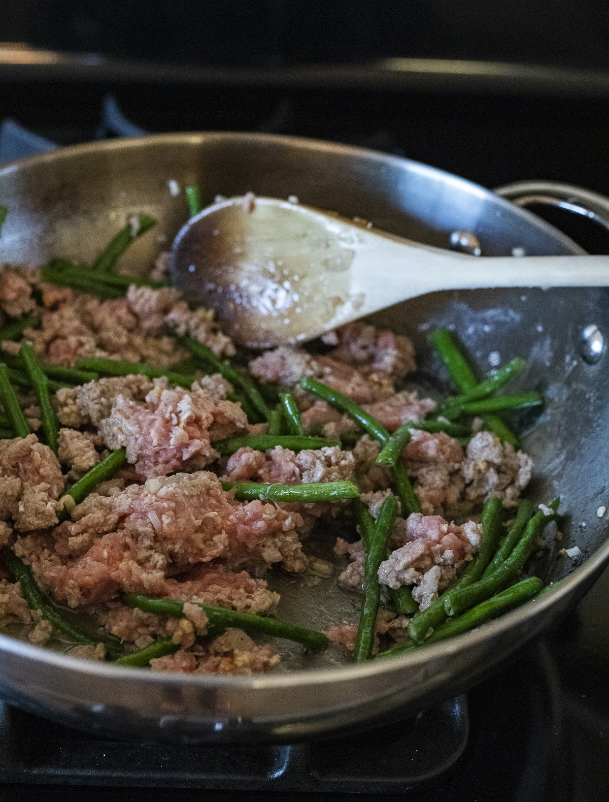 Ground pork being cooked with long beans in a wok.
