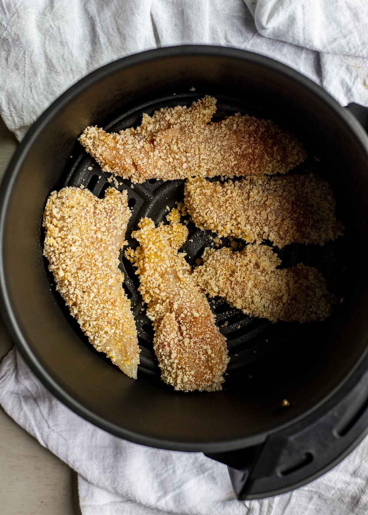 Breaded chicken tenders in an air fryer basket.
