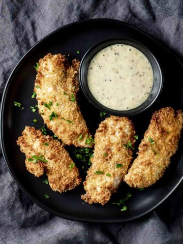 Air fried chicken tenders on a black plate with a small bowl of dijon sauce.