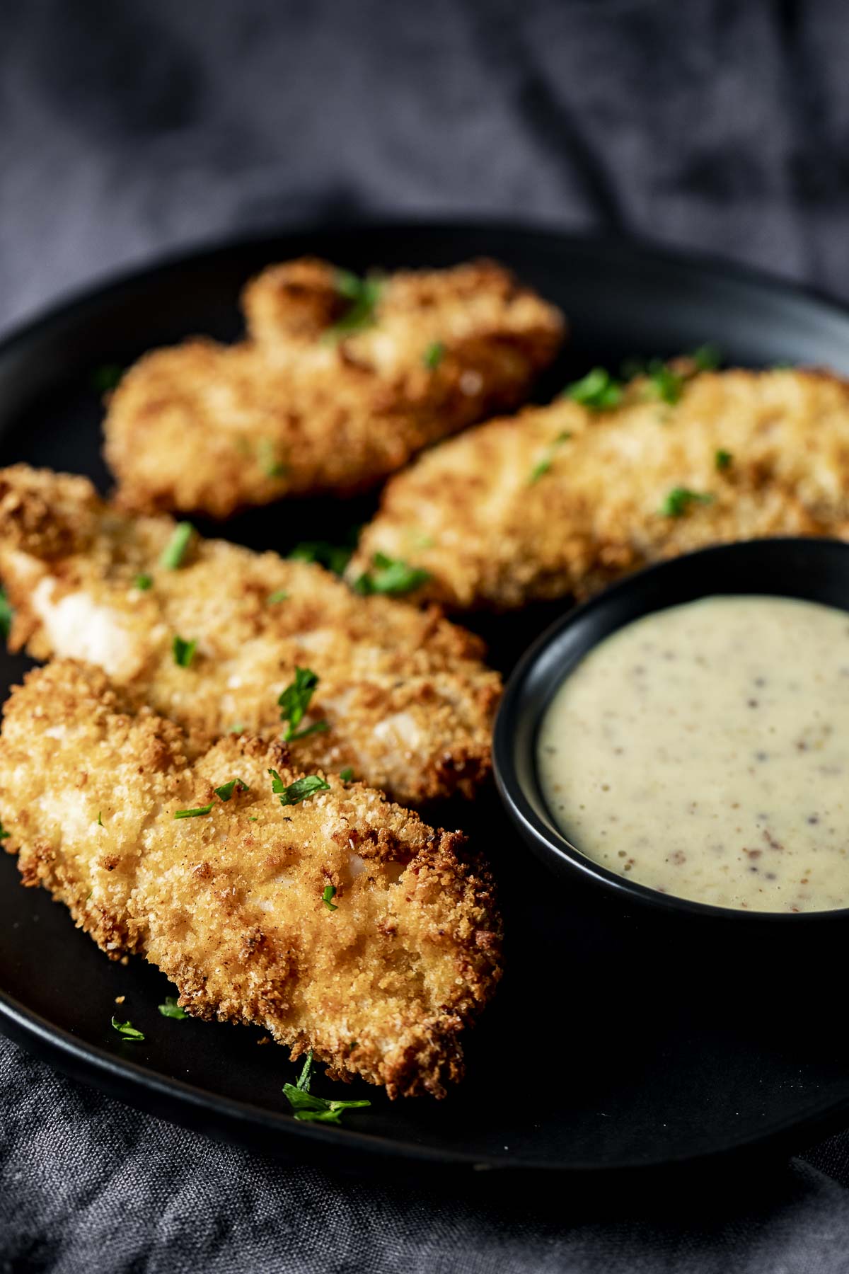 Side view of chicken tenders next to a bowl of creamy dijon sauce.