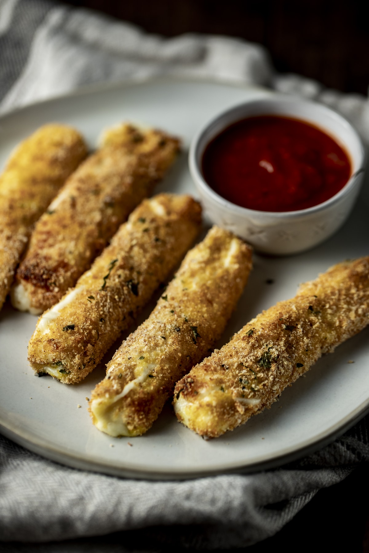 Side view of mozzarella sticks on a plate with marinara sauce.