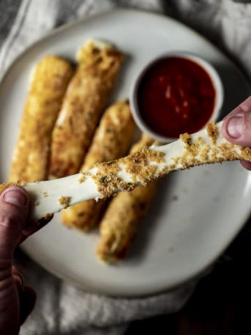 Close up view of a mozzarella stick being pulled apart to expose the stretchy cheese.