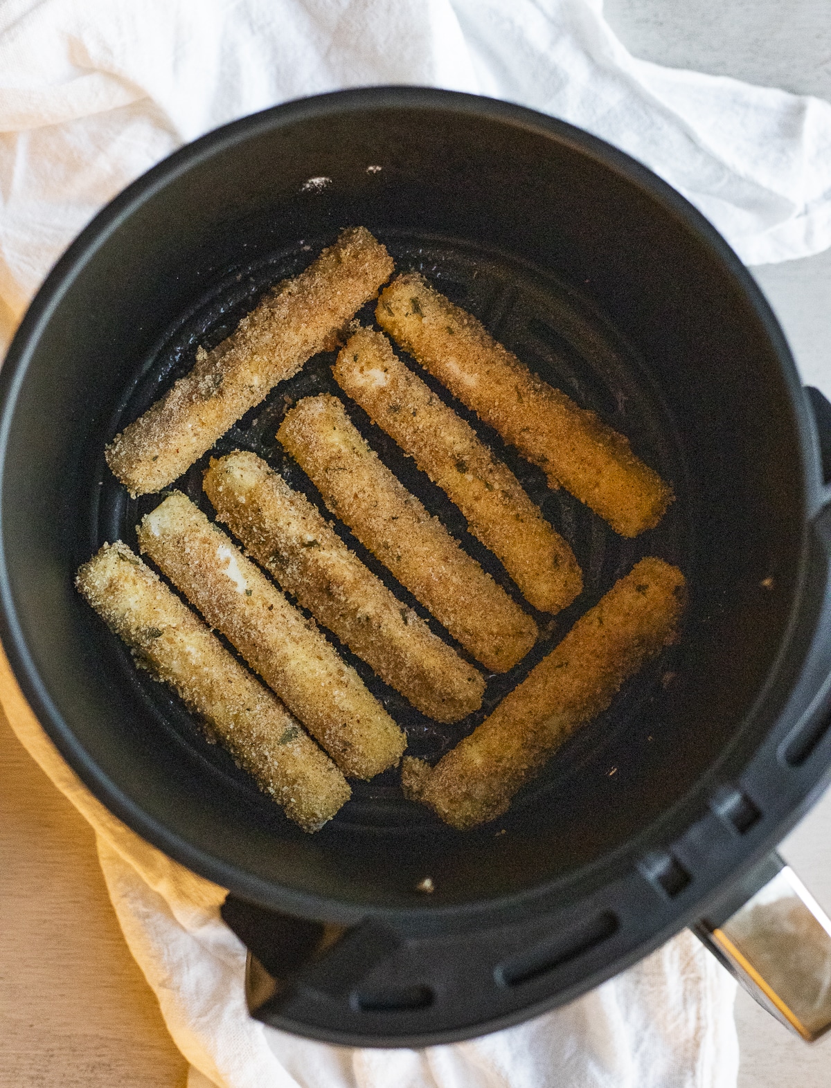 Breaded mozzarella sticks arranged in a single layer in an air fryer basket.