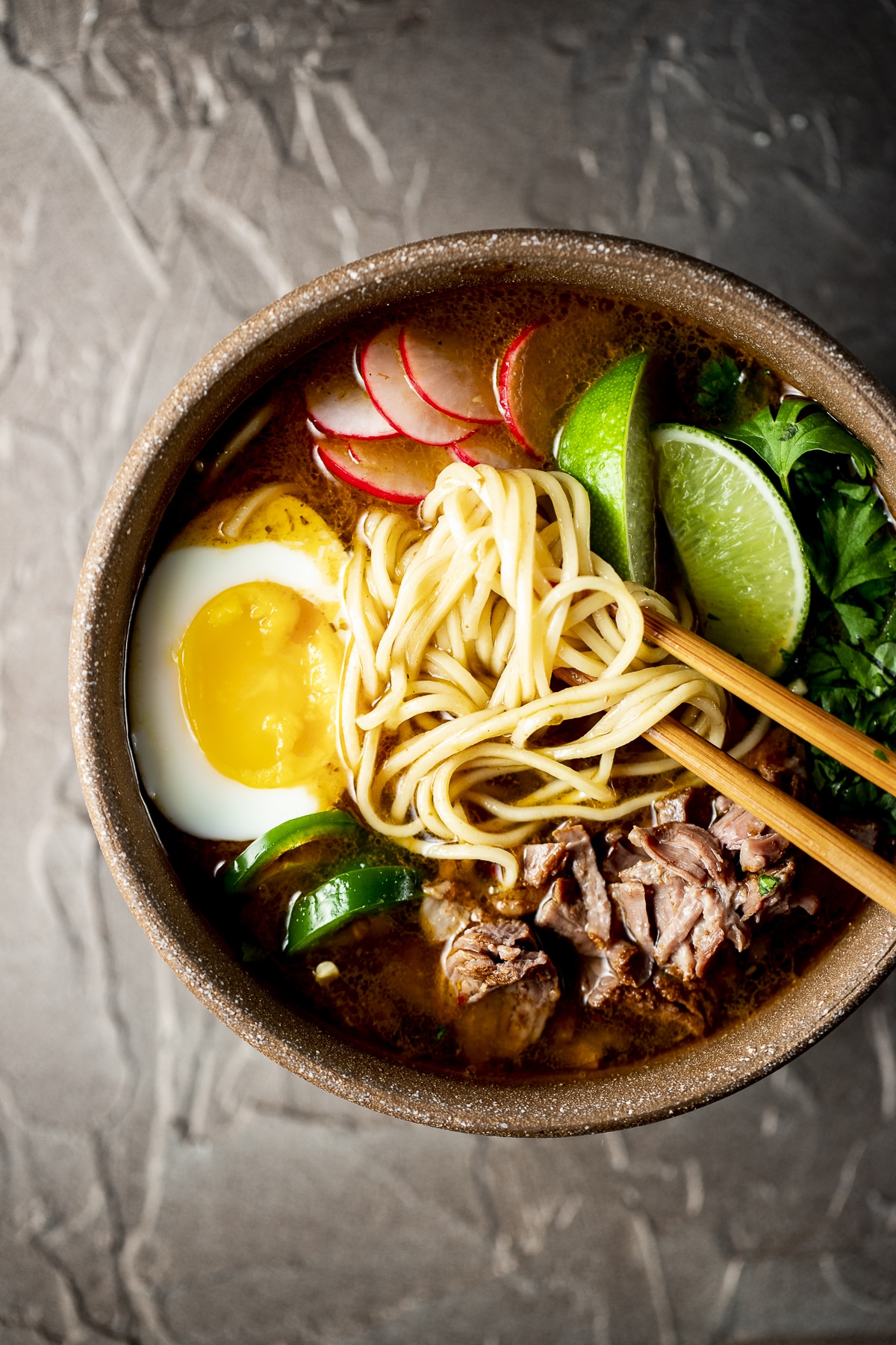 Overhead view of birria ramen in a bowl with chopsticks inserted into it.