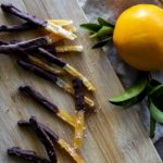 sliced orange peels coated in chocolate with an orange on the side