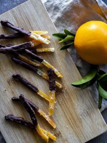 sliced orange peels coated in chocolate with an orange on the side