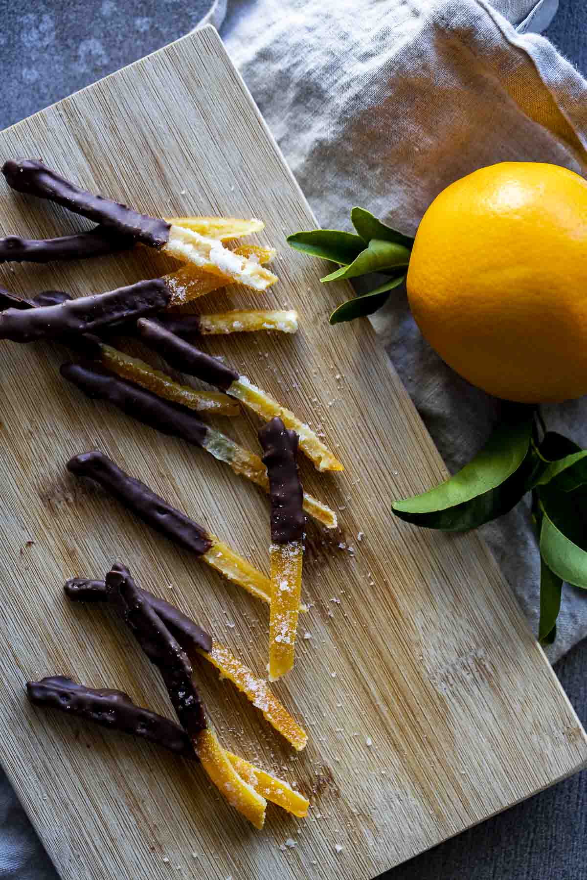 sliced orange peels coated in chocolate with an orange on the side