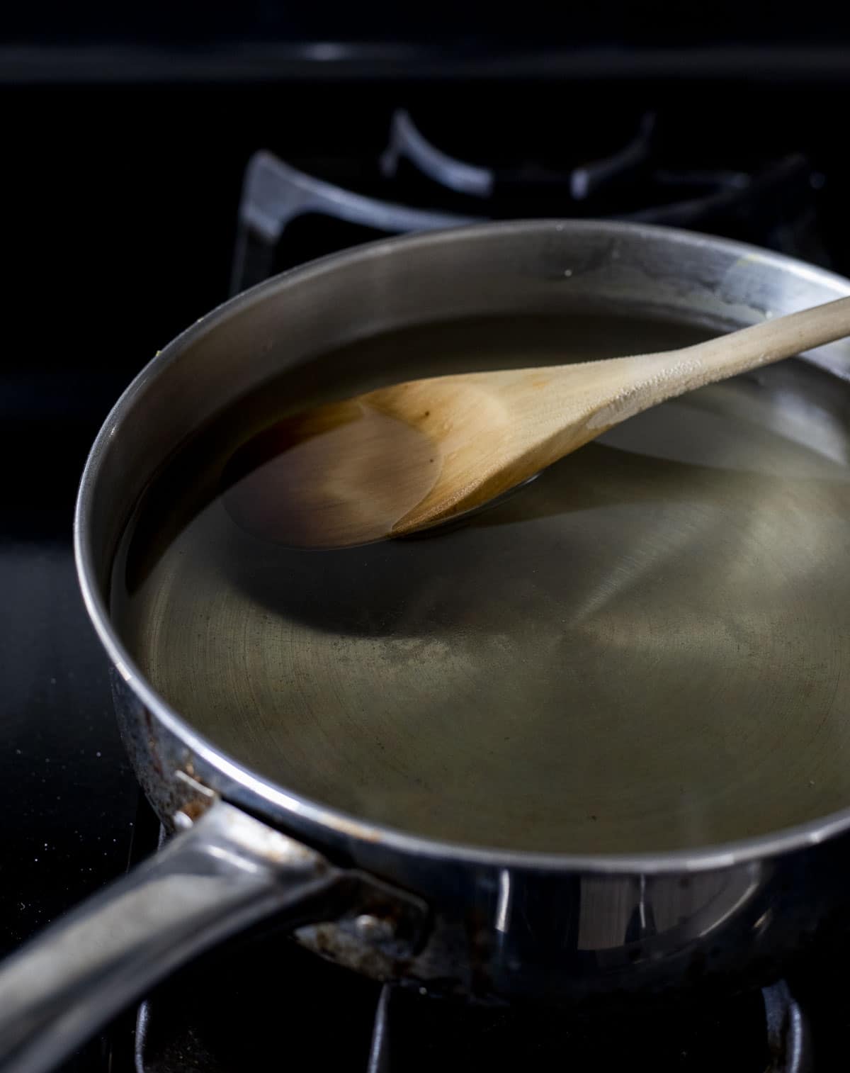 Sugar water in a high-sided skillet with a wooden spoon inserted into it.
