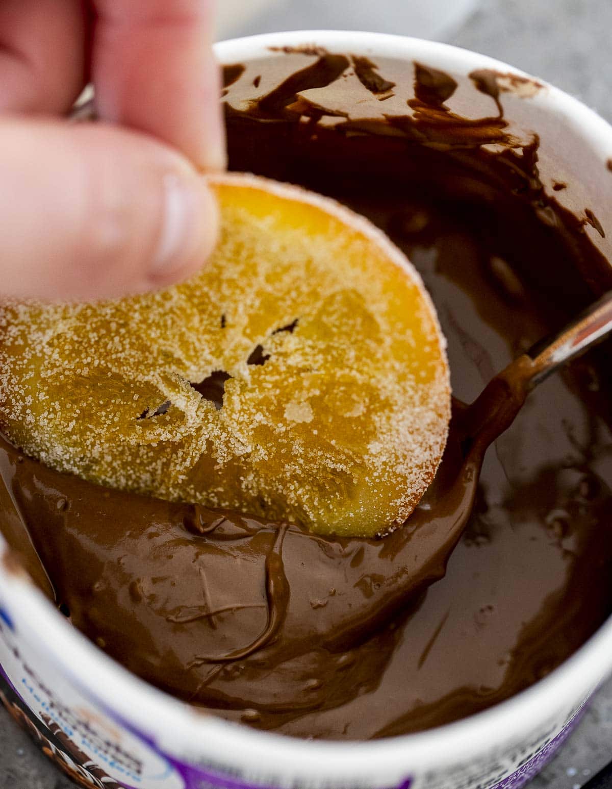 A sugar coated orange slice being dipped in chocolate.