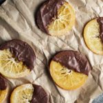 Chocolate dipped candied orange slices arranged on brown paper.