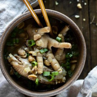 a bowl of chicken feet in broth with chopsticks garnished with green onions